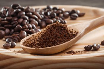 Ground coffee in wooden spoon. Coffee fried grain on wooden platter. Close-up. Coffee ground, coffee beans.